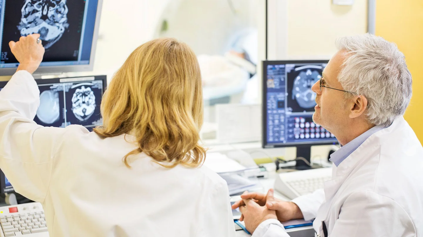 Epilepsie: Eine &Auml;rztin und ein Arzt begutachten das gescannte Bild eines Sch&auml;dels und Gehirns auf einem Monitor.
