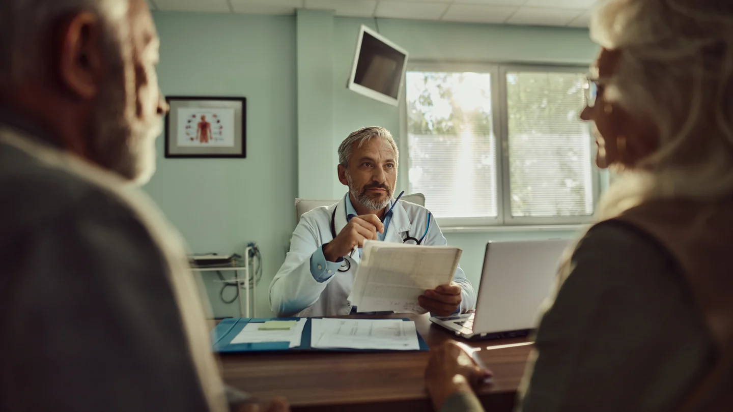 Mann und Frau im Gespräch mit einem Arzt im Arztzimmer. 