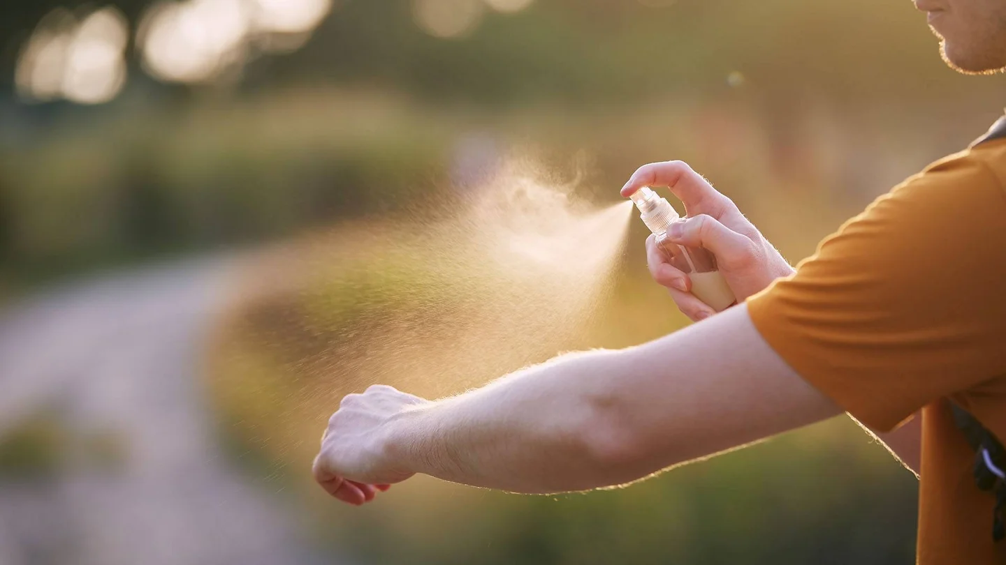 Person spr&uuml;ht sich mit M&uuml;ckenschutzspray ein.