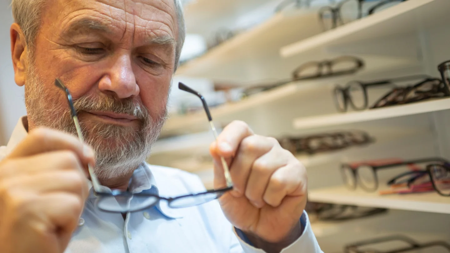 Alterssichtigkeit: Ein älterer Mann begutachtet eine Brille, die er in seinen Händen hält.