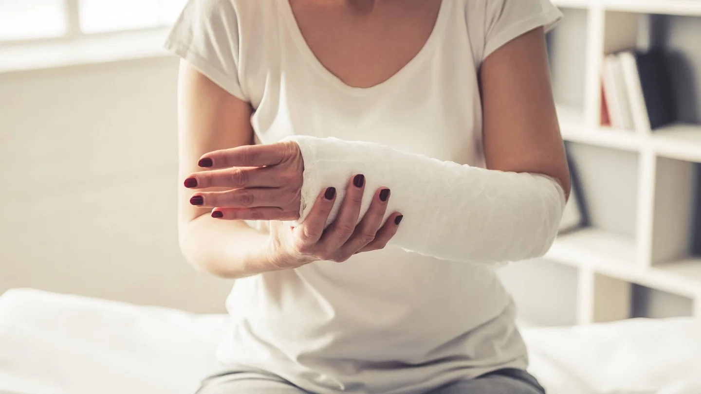 Nahaufnahme einer Frau mit geschientem Unterarm, die auf einer Behandlungsliege sitzt.