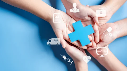 Mehrere Hände liegen übereinander und halten ein Kreuz, das das Gesundheitswesen symbolisiert. Darum herum sind Symbole gruppiert, die für Leistungen der Krankenversicherung stehen. 