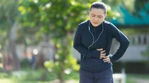 Eine junge Frau in Joggingkleidung ist drau&szlig;en stehengeblieben und h&auml;lt sich die linke Bauchseite.