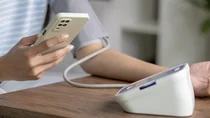 Eine Person misst ihren Blutdruck und schaut dabei auf ihr Smartphone.