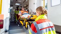 Eine Sanit&auml;terin schiebt einen Patienten, der auf einer Trage liegt, in den Krankenwagen.