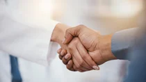 Verbindlicher H&auml;ndedruck zwischen einer Person im Kittel und einer Person im Hemd.