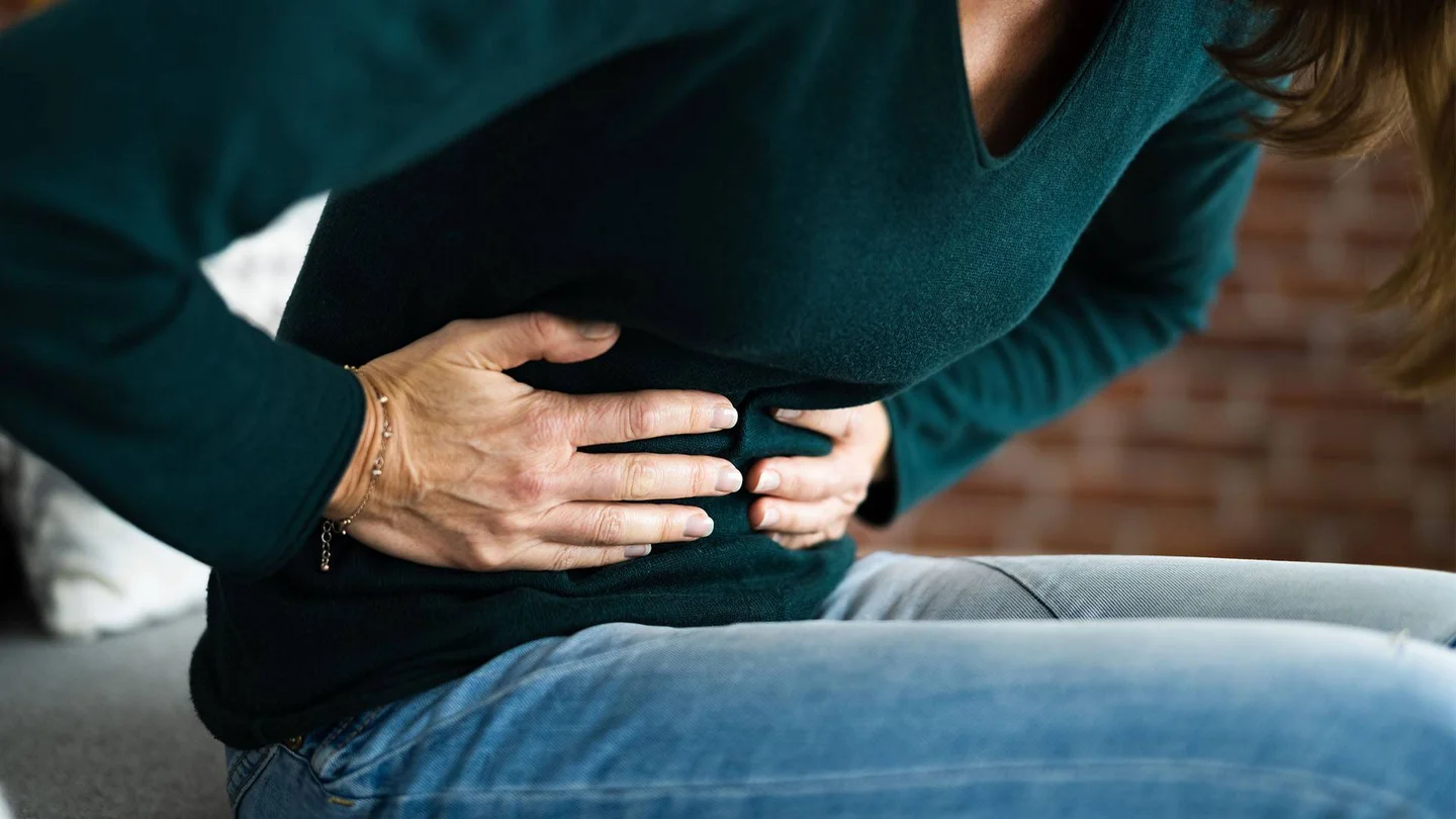 Eine Frau fasst sich mit beiden H&auml;nden auf die Bauchdecke.