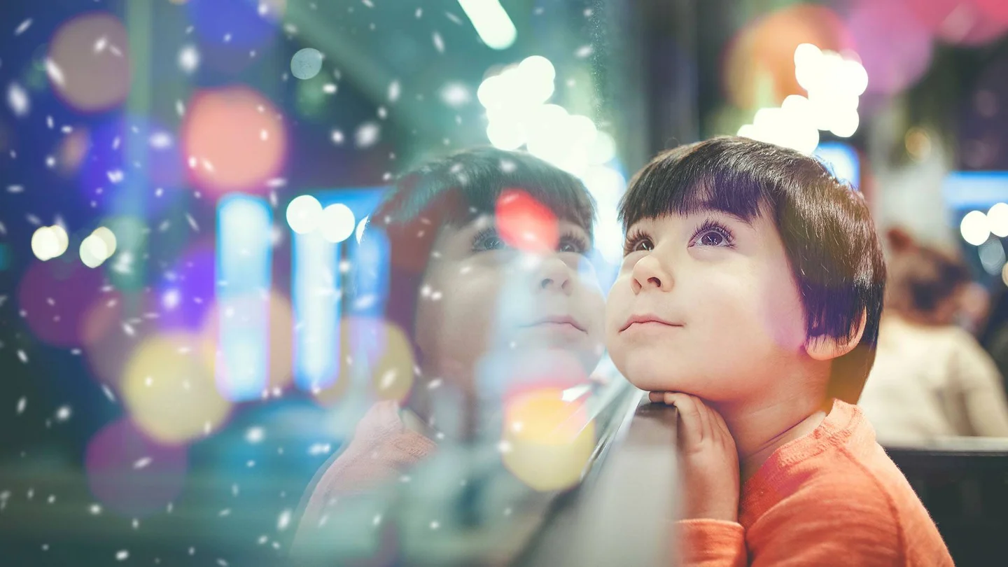 Kind lehnt an einer Fensterscheibe und guckt verträumt.