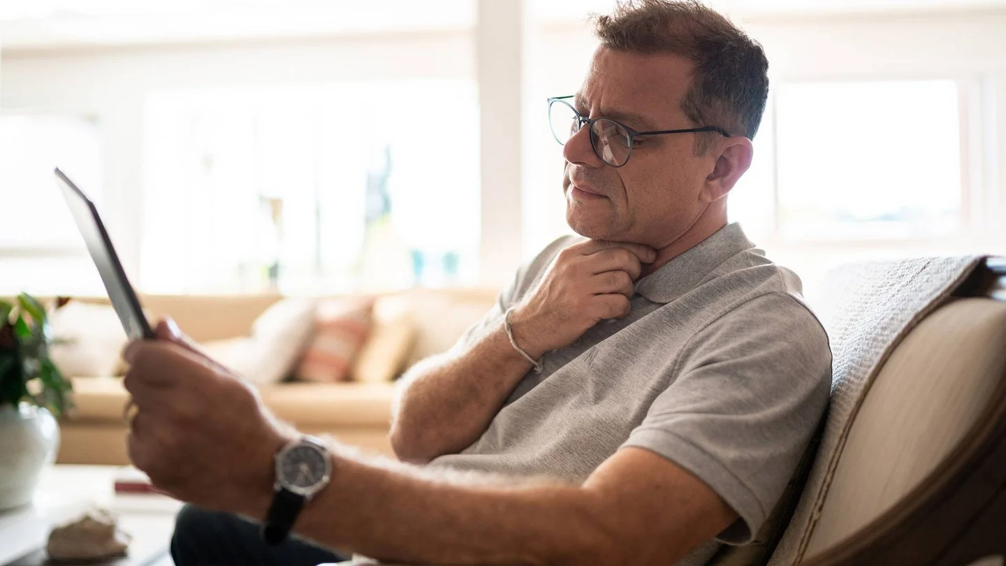 Mann mittleren Alters fasst sich an den Kehlkopf