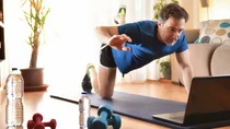 Ein Mann macht auf der Yogamatte &Uuml;bungen vor seinem Laptop.