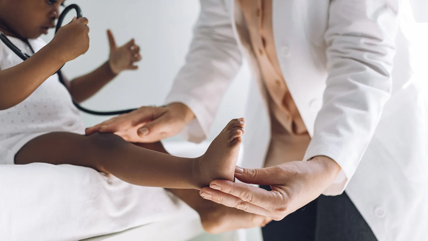 Gesundheitsuntersuchungen für Kinder und Jugendliche: Ein kleines Kind sitzt auf einer Arztliege und spielt mit einem Stethoskop. Eine Ärztin untersucht das Kind vorsichtig.