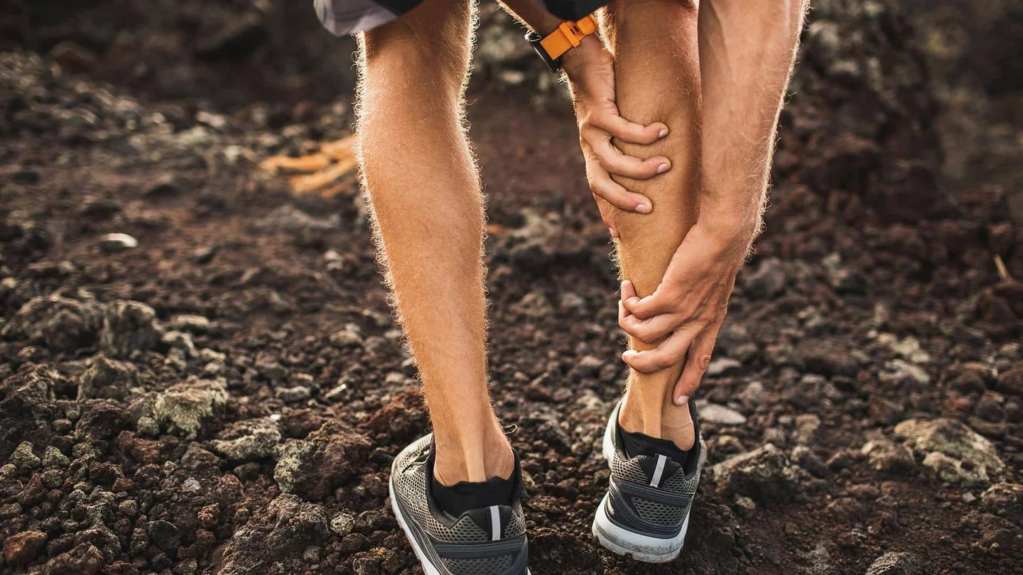 Eine Person in Sportkleidung b&uuml;ckt sich und fasst sich an die vermutlich schmerzende Wade.