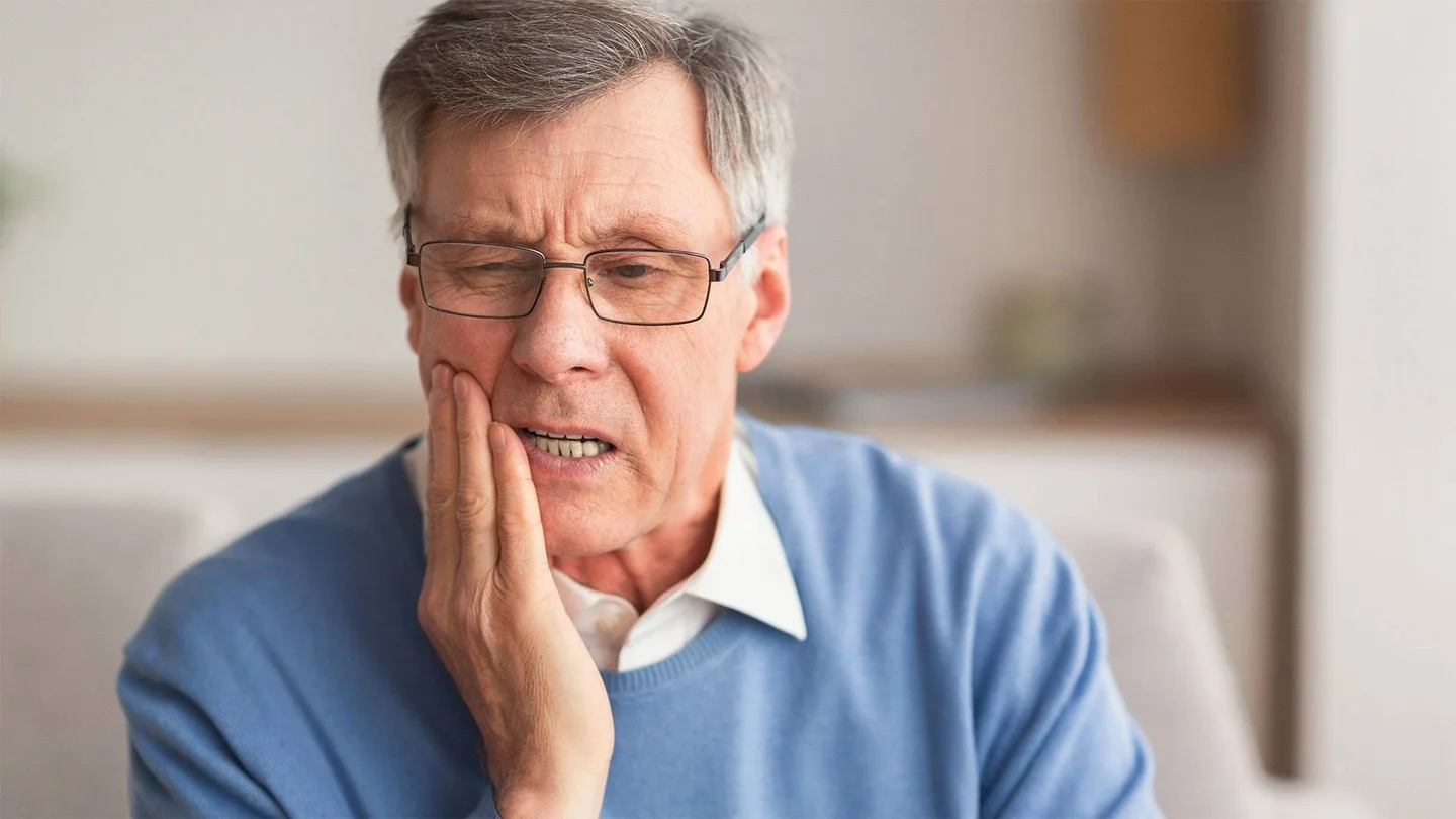 Ein gepflegter &auml;lterer Herr fasst sich besorgt an die rechte Wange; sein Gesicht ist schmerzverzerrt.