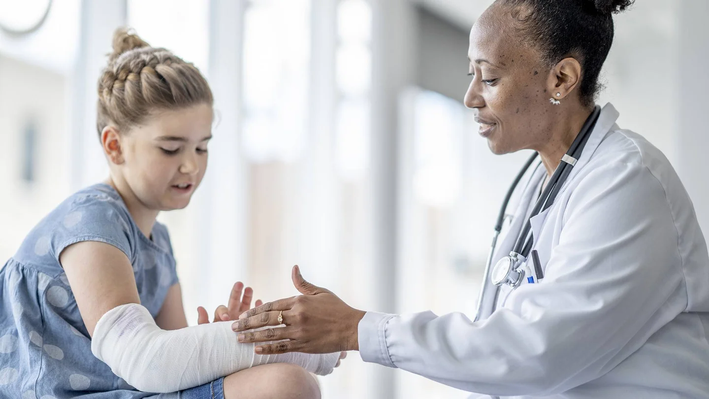 Eine &Auml;rztin pr&uuml;ft den eingegipsten Arm eines M&auml;dchens.