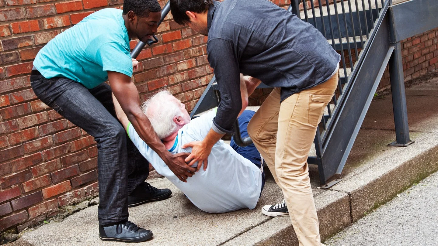 Ein Senior ist auf der Treppe gest&uuml;rzt. Zwei M&auml;nner helfen ihm auf.
