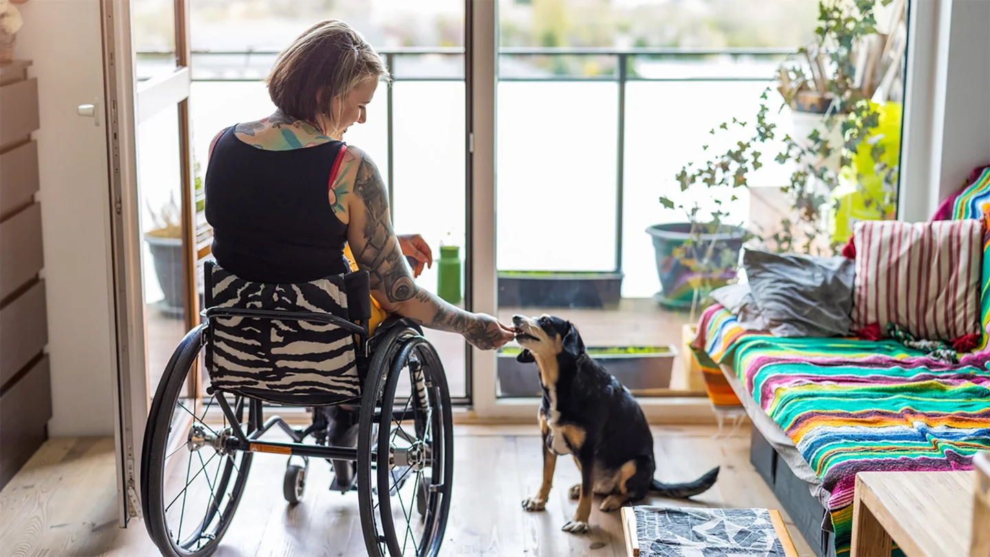 Eine Frau im Rollstuhl f&uuml;ttert einen Hund.
