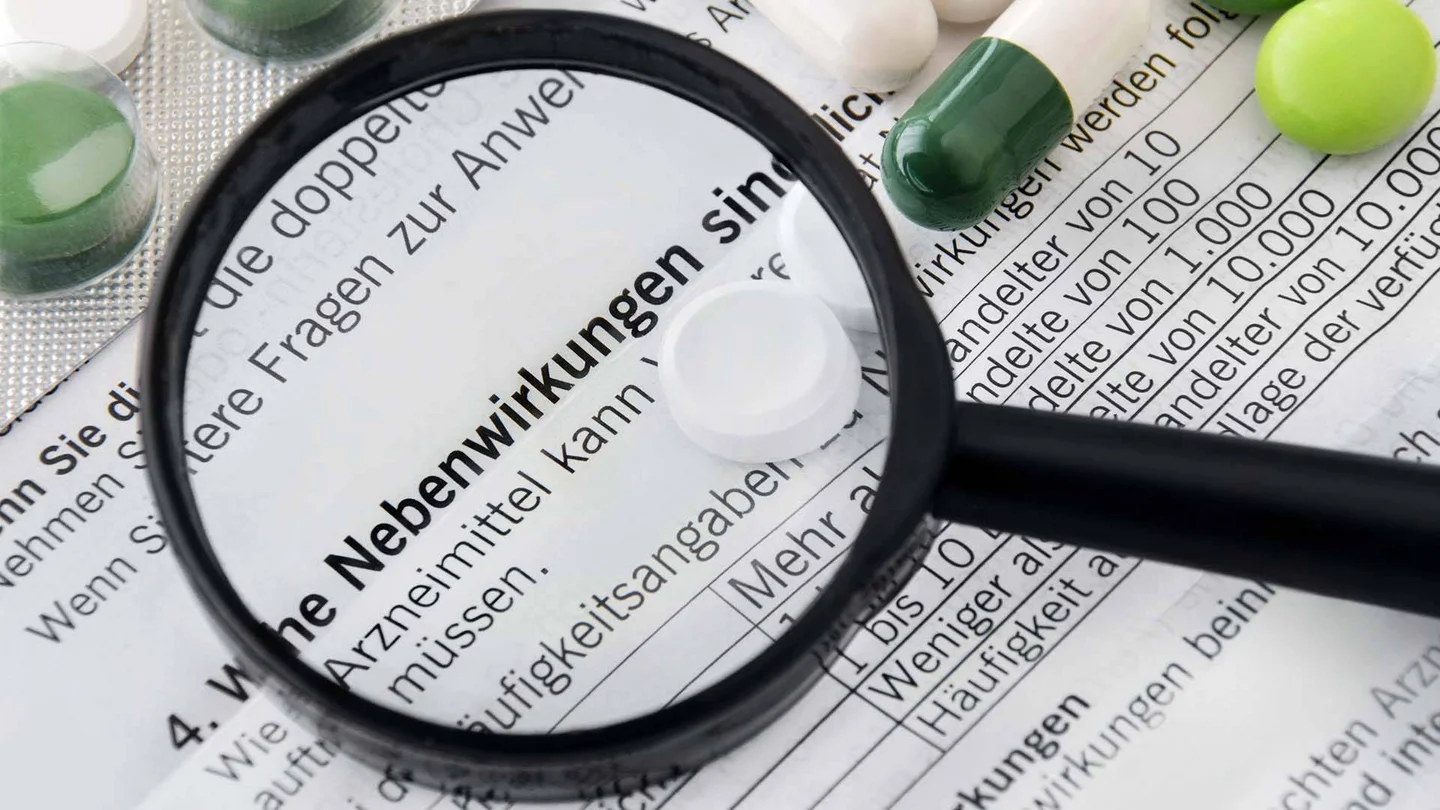 Ausschnitt eines Beipackzettels, auf dem einige Tabletten liegen. Der Satz &bdquo;Welche Nebenwirkungen sind m&ouml;glich?&ldquo; wird unter einer Lupe vergr&ouml;&szlig;ert.