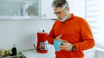 Ein Mann mit Gastritis h&auml;lt eine Kaffeetasse in der Hand und fasst sich an den schmerzenden Bauch.
