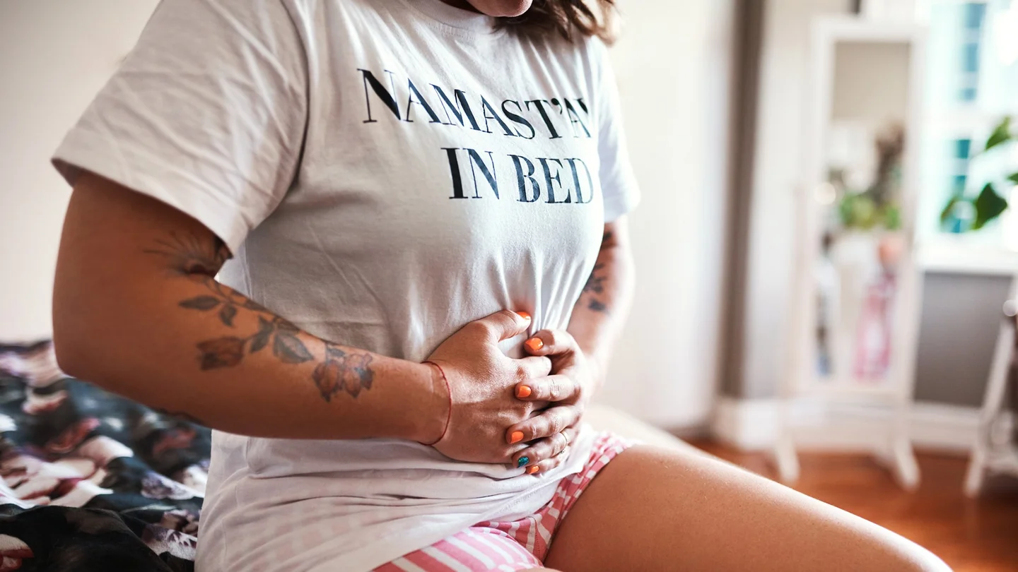 Ovarialzysten: Eine Frau sitzt auf einem Bett und h&auml;lt sich mit beiden H&auml;nden den Bauch.