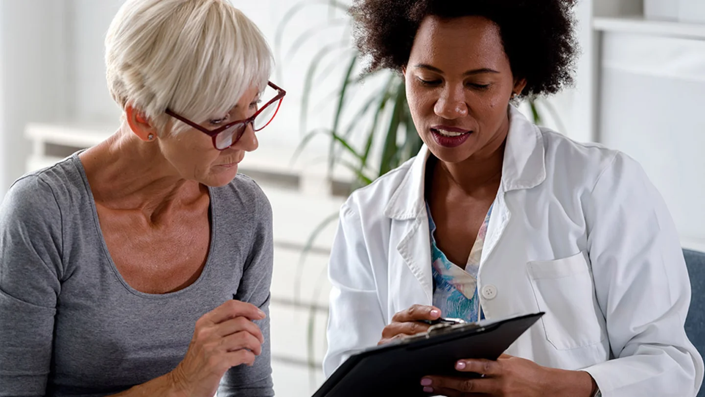 Eine &Auml;rztin erkl&auml;rt einer Patientin etwas und zeigt dabei auf ihre Unterlagen. 