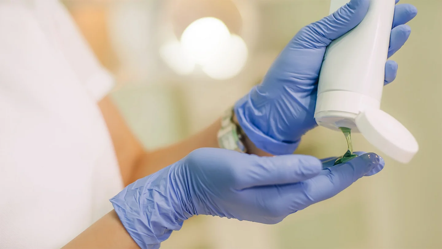 Eine Frau mit Einmalhandschuhen tr&auml;gt ein Gel auf. 