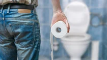 Ein Mann steht mit Toilettenpapier vor einer Toilette