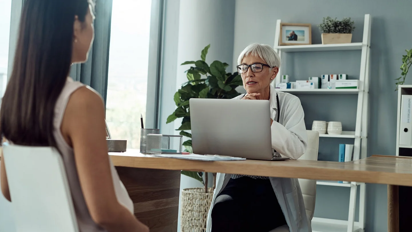 Eine Frau sitzt in einem Behandlungszimmer. Ihr gegen&uuml;ber sitzt eine &Auml;rztin und guckt auf ihren Laptop.