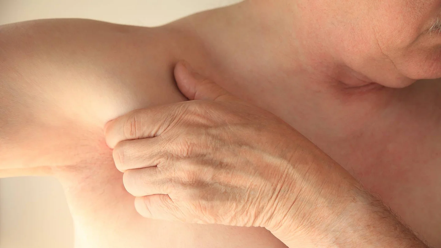 Ein Mann mit freiem Oberk&ouml;rper streckt seinen rechten Arm zur rechten Seite aus. Mit der linken Hand umgreift er seine Achselh&ouml;hle.